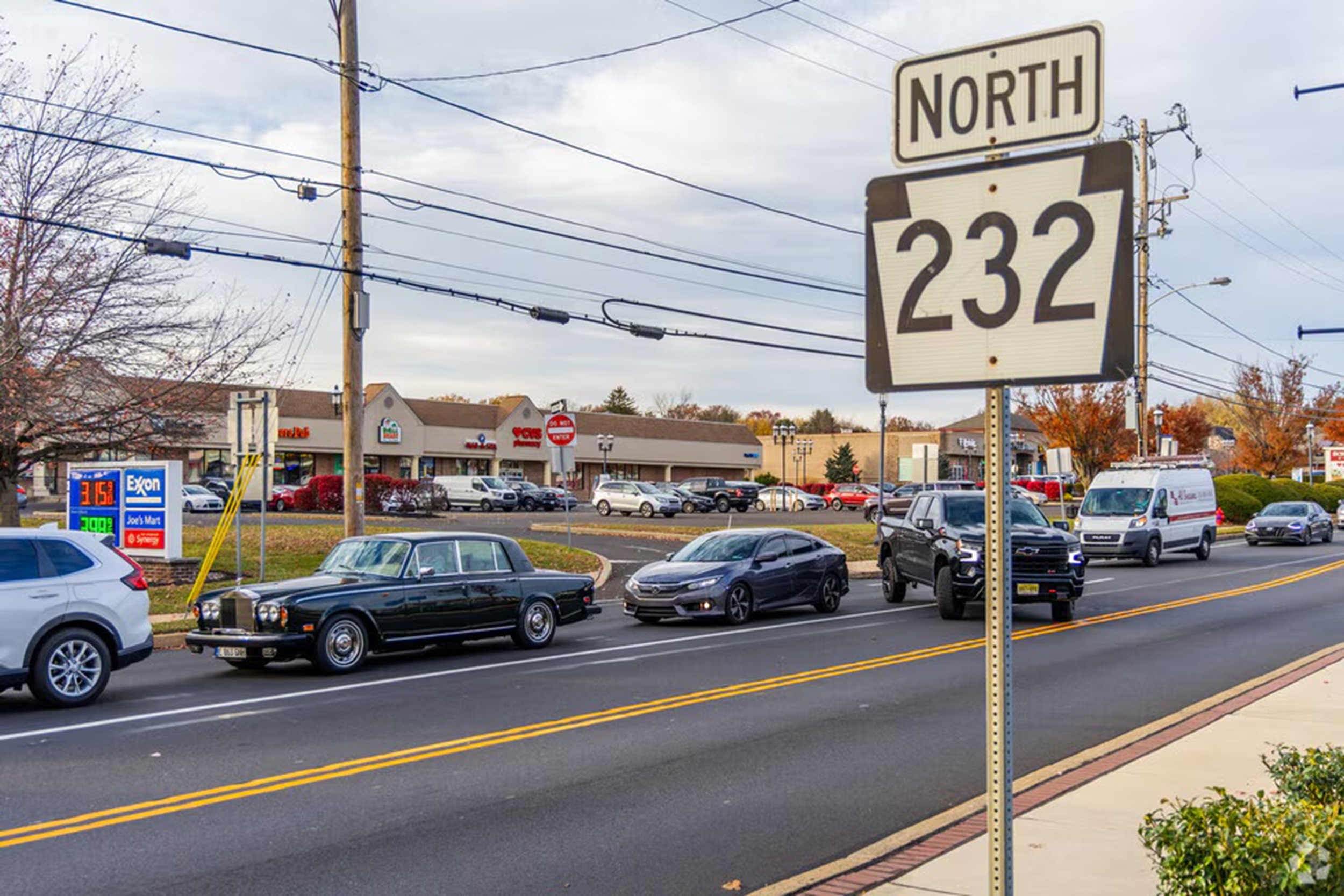 Busy street scene with a large North 232 highway sign, power lines, and parked cars in front of stores.