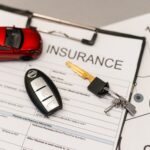 Auto insurance documents on a desk with a red toy car and car keys nearby, suggesting an auto insurance setup or quote.