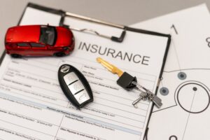 Auto insurance documents on a desk with a red toy car and car keys nearby, suggesting an auto insurance setup or quote.
