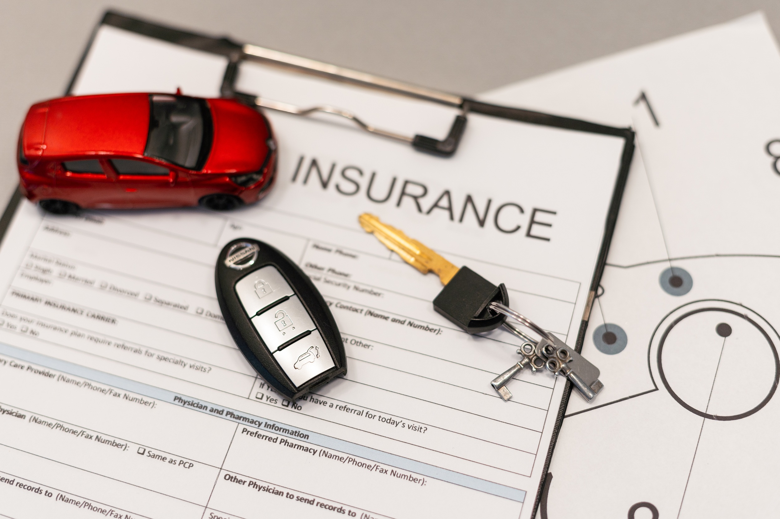 Auto insurance documents on a desk with a red toy car and car keys nearby, suggesting an auto insurance setup or quote.